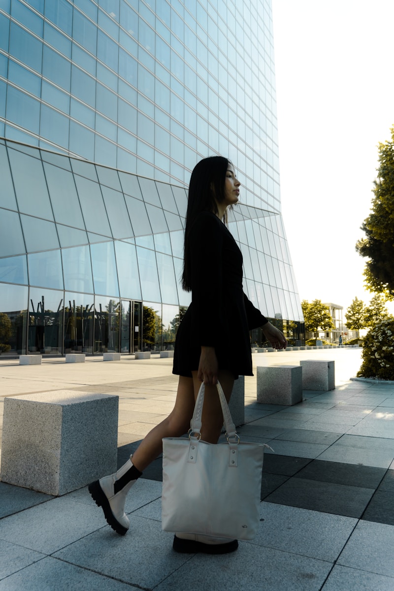 a woman walking down a sidewalk carrying a white bag